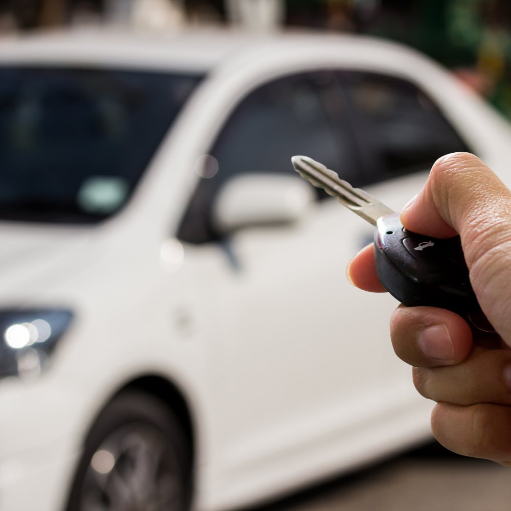 Hand holding a car key in front of a white car