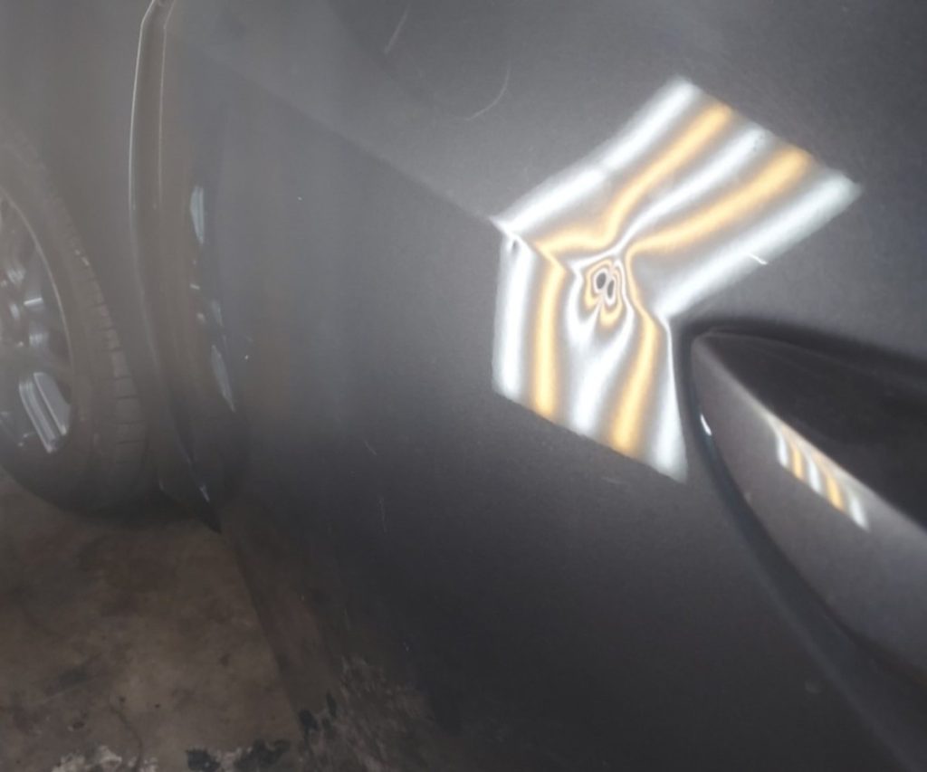 Dent beside a door handle under a reflection board before paintless dent repair