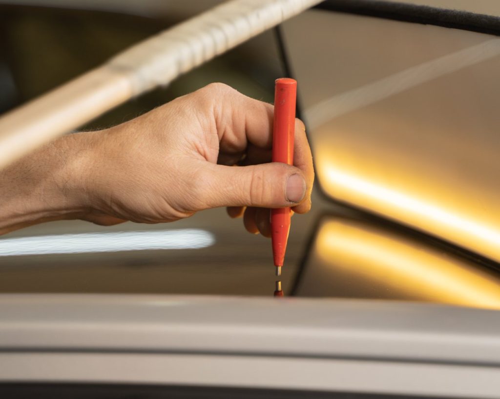 Technician holding a dent repair tool under a light board on a silver car