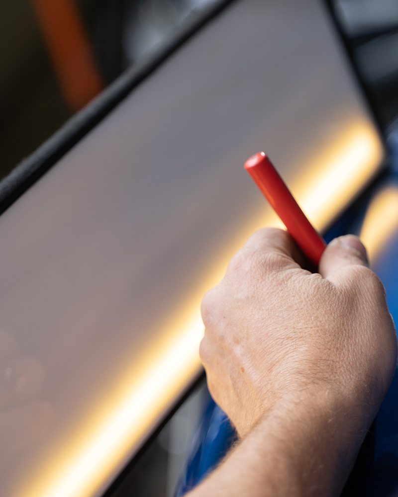 Technician marking a dent on a blue car under a light board